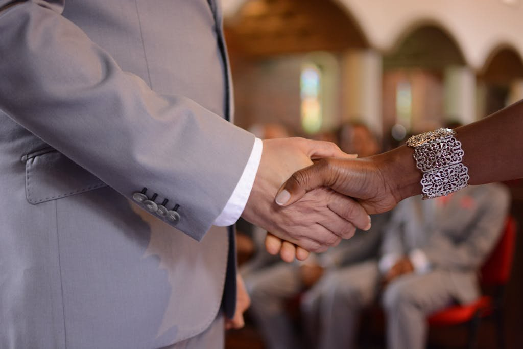 A close-up of an elegant handshake during a formal ceremony indoors, focusing on attire and jewelry.