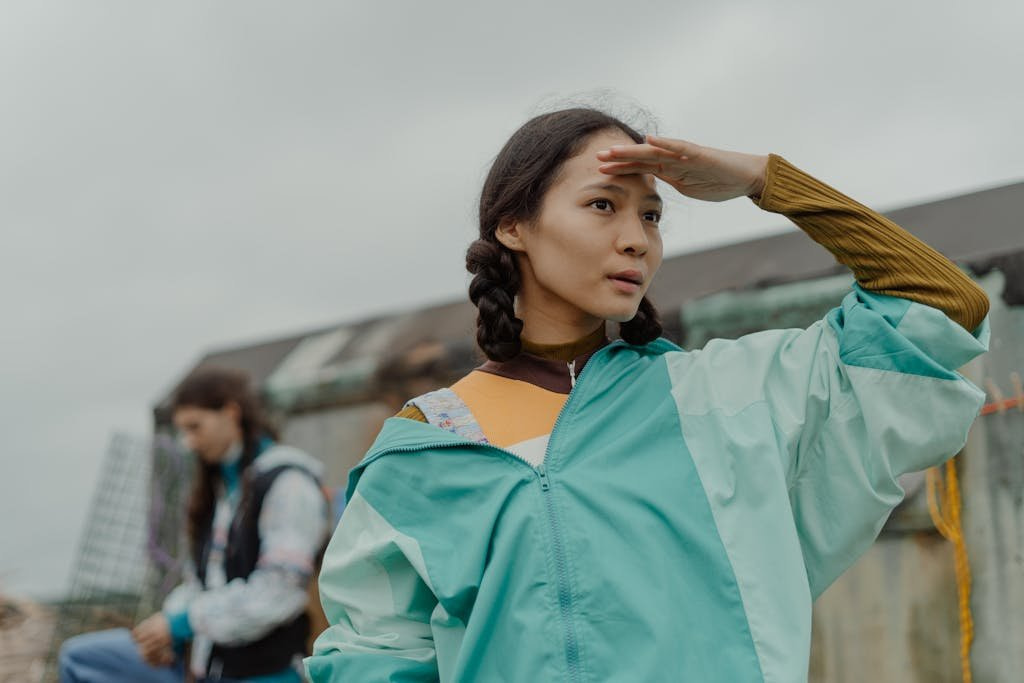 Young woman with braided hair in blue jacket looking into distance outdoors.